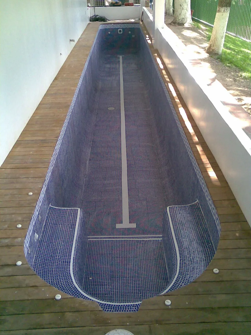 Carril de nado alargado con acabado en mosaico azul y grecas, sobre deck de madera