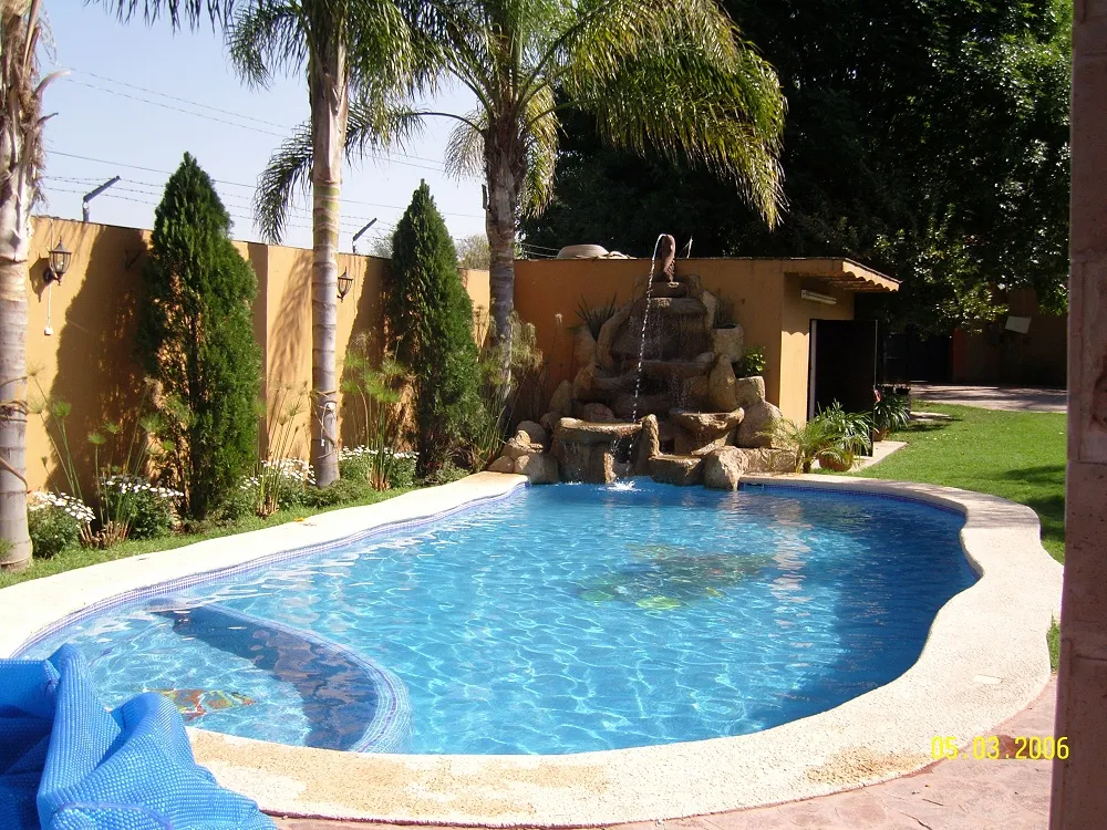 Piscina residencial con cascada de roca artificial y enrollador de cubierta térmica