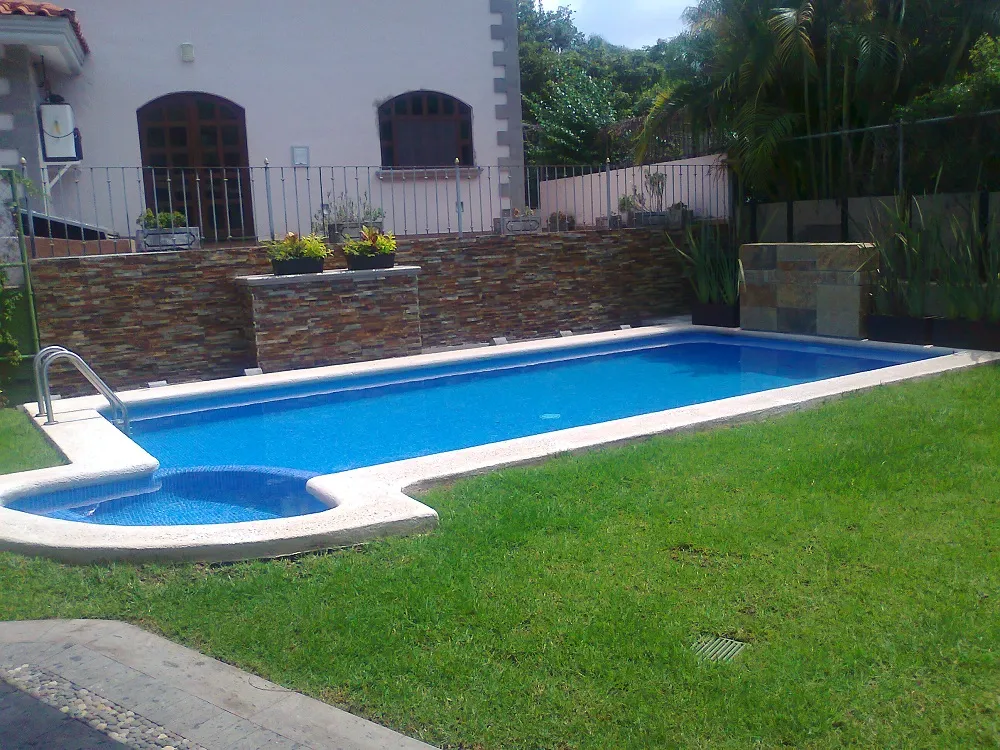 Piscina rectangular con jacuzzi integrado en una esquina y muro de piedra al fondo