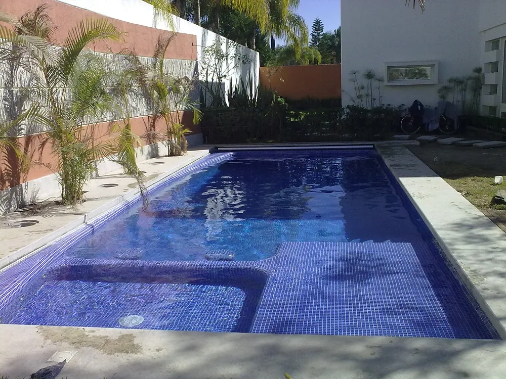 Piscina residencial con acabado en mosaico azul cobalto, banca sumergida y cubierta automática