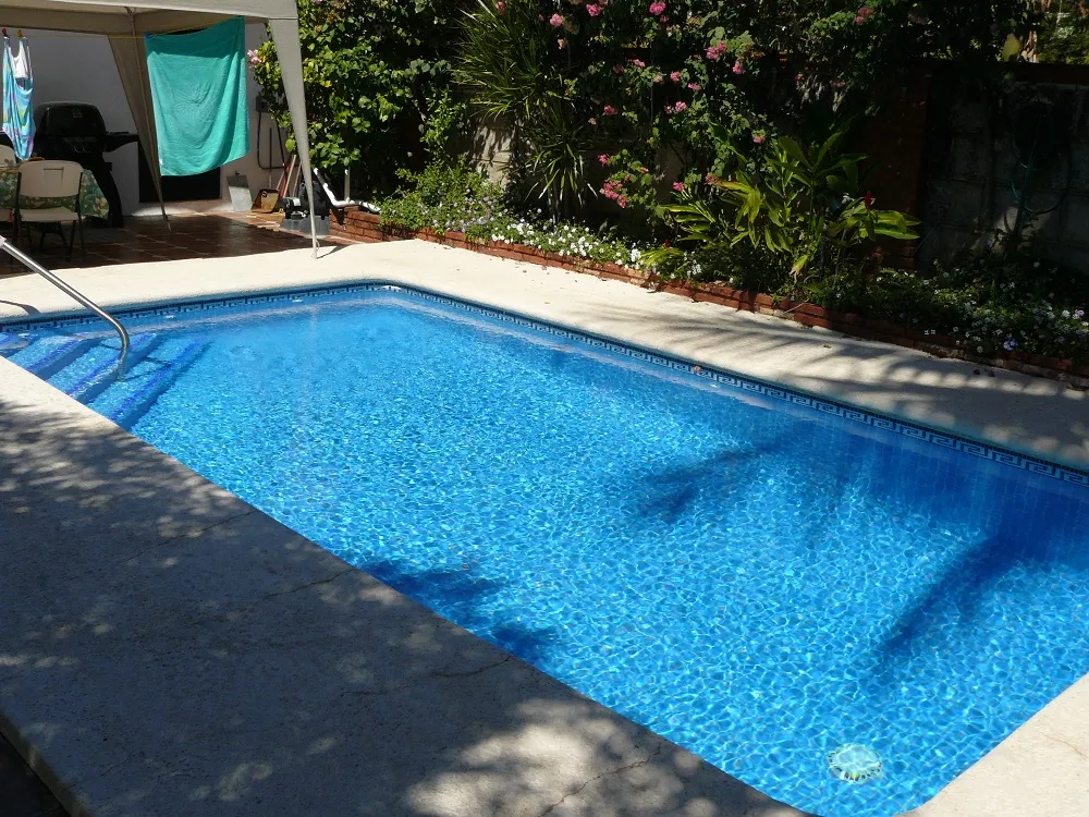 Alberca residencial rectangular con greca de mosaico y jardín florido alrededor