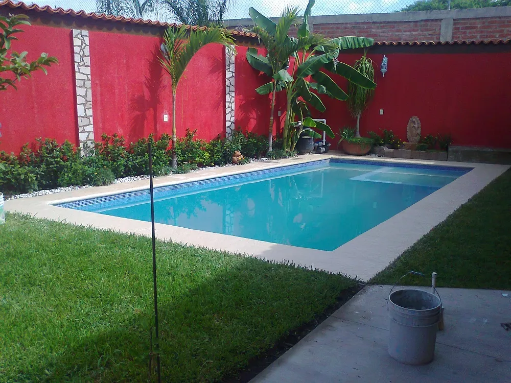 Alberca residencial con banca sumergida, jardín y muro rojo al fondo
